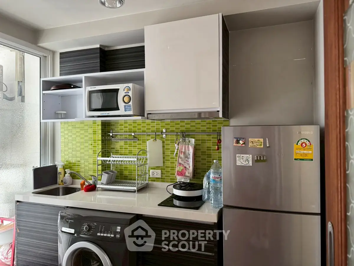 Modern kitchen with green backsplash, stainless steel fridge, and washing machine, ideal for compact living spaces.
