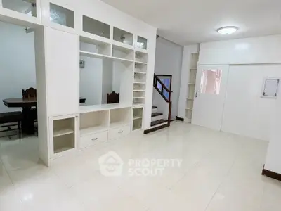 Spacious living area with built-in shelving and modern staircase in a bright home.