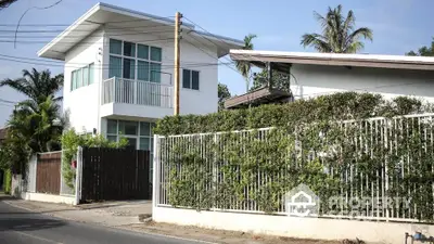 Charming two-story home with a lush green hedge fence, offering privacy and a serene living environment in a tropical setting.