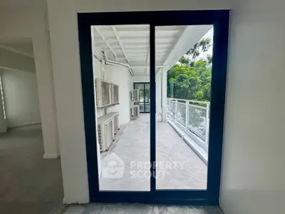 Spacious balcony with sliding glass doors and lush greenery view.