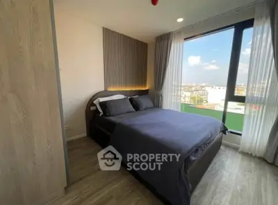 Modern bedroom with large window and city view, featuring stylish decor and cozy bedding.