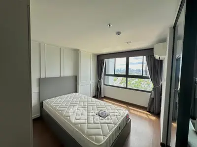 Spacious bedroom with large window offering stunning city views, featuring a comfortable bed and modern decor.