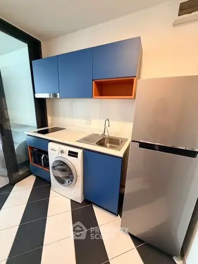 Modern kitchen with blue cabinets, washing machine, and stainless steel fridge