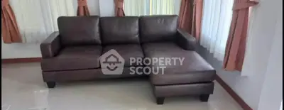 Cozy living room with elegant brown leather sofa and natural light from large windows.