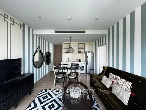Stylish modern living room with open kitchen, featuring chic decor and striped walls.