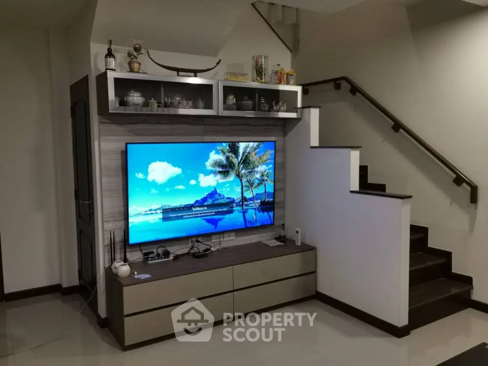 Modern living room with sleek TV unit and stylish staircase design.