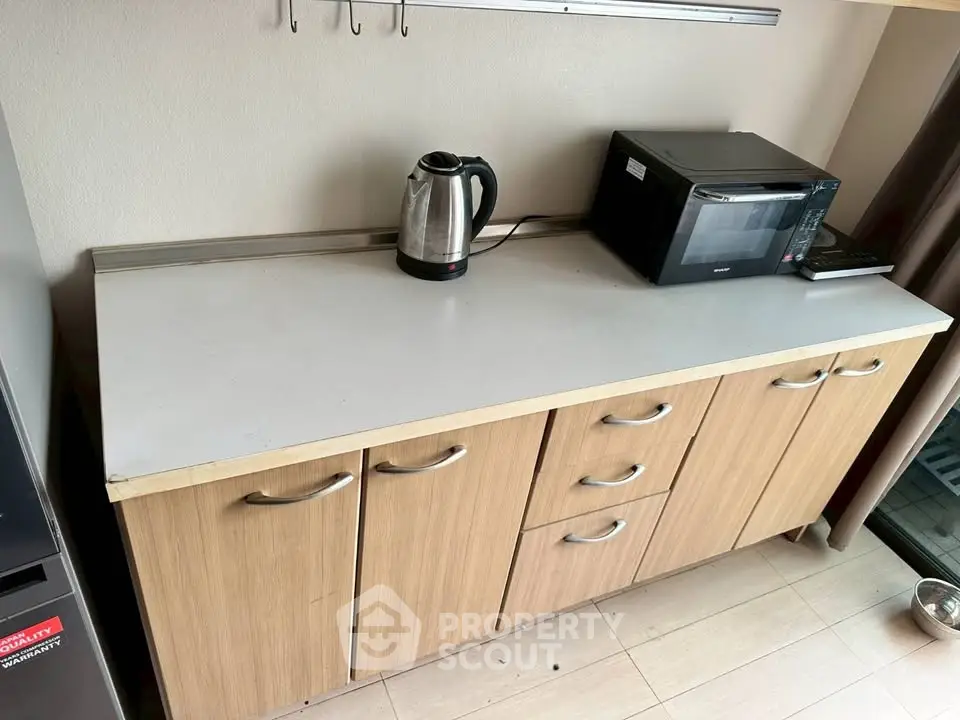 Modern kitchen with wooden cabinets, microwave, and kettle on a sleek countertop.