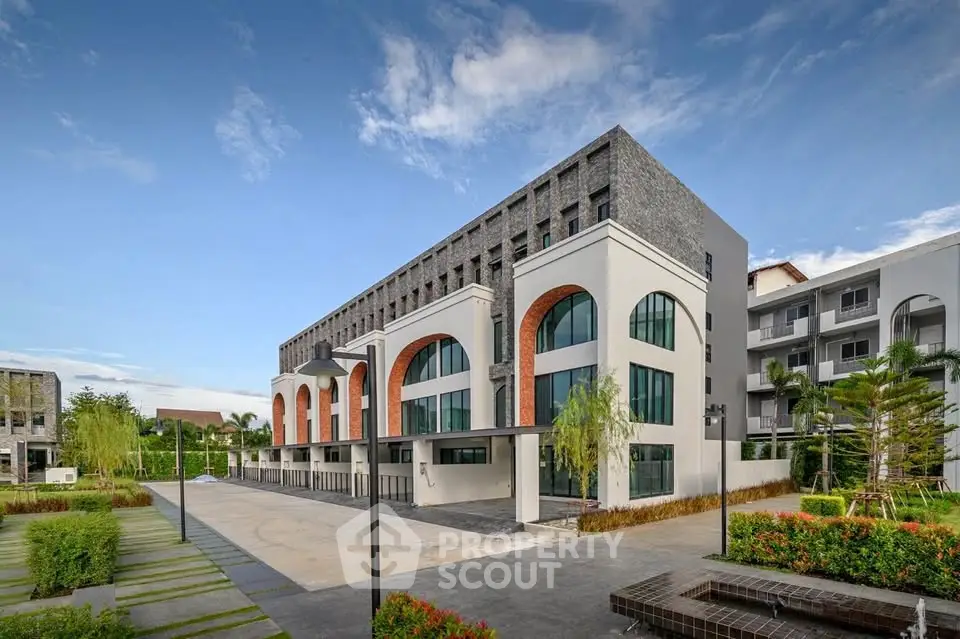 Modern architectural building with lush landscaping and clear blue sky, showcasing contemporary design and spacious surroundings.