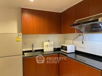 Modern kitchen with sleek wooden cabinets and black countertops, featuring a microwave and stainless steel range hood.