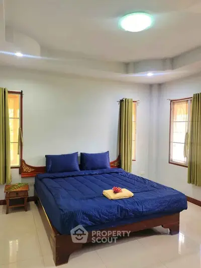 Spacious bedroom with elegant blue bedding and natural light from large windows.