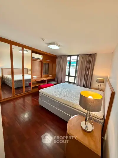 Spacious bedroom with wooden flooring and large mirrored wardrobe in modern apartment.