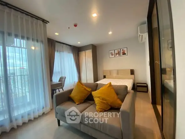 Modern studio apartment with cozy living area and large windows for natural light.