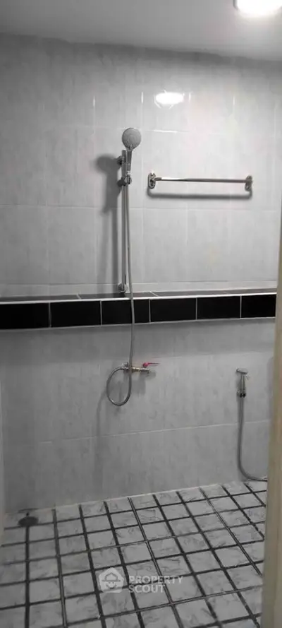 Modern bathroom with tiled walls and floor, featuring a shower and towel rack.