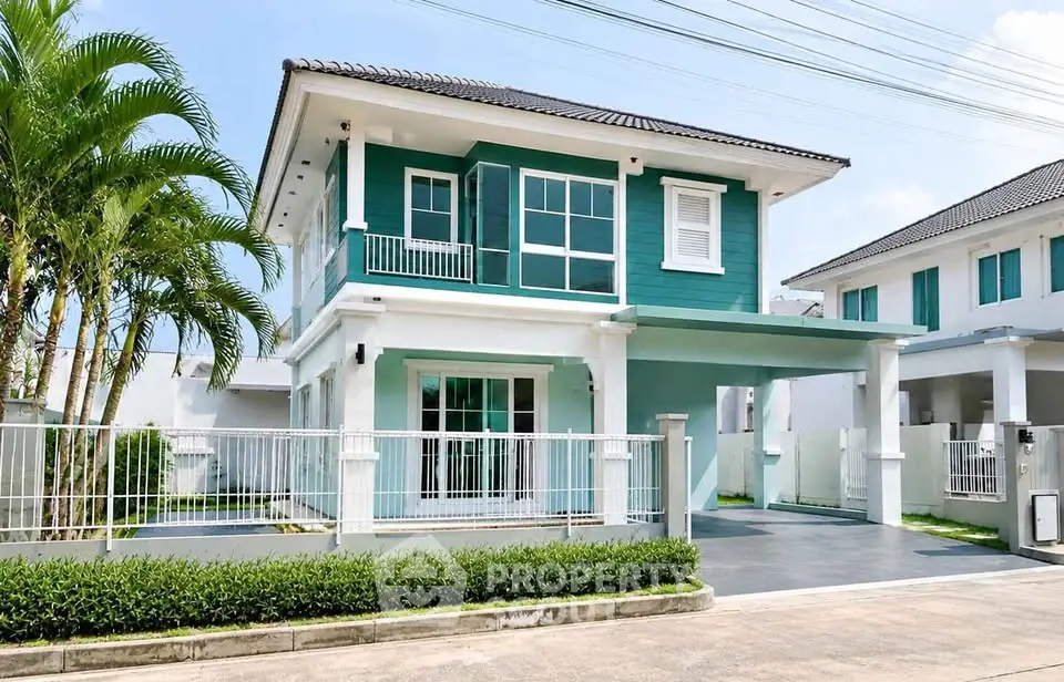 Charming two-story teal house with modern design and lush greenery, perfect for family living.