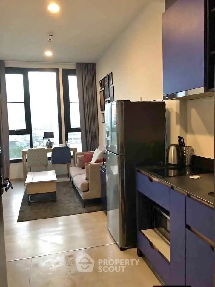 Modern open-plan living room with kitchen, featuring stylish furniture and large windows.