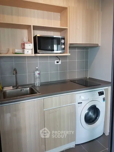 Modern compact kitchen with wooden cabinets, microwave, washing machine, and sleek countertop.