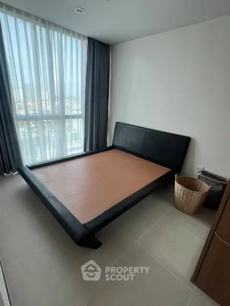 Spacious bedroom with large window and modern bed frame, offering city views.