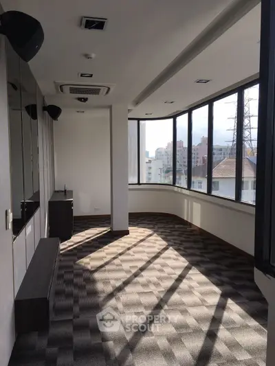 Spacious sunlit room with large windows and city view, perfect for office or creative space.