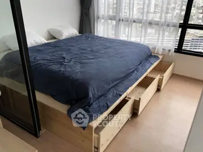 Spacious bedroom with large bed and storage drawers, featuring city view through large windows.
