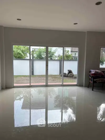 Spacious living room with large windows offering garden view and glossy tiled flooring.