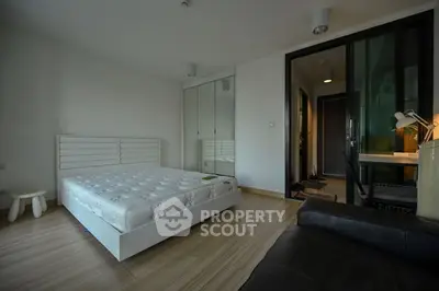 Modern bedroom with minimalist design, featuring a sleek bed, mirrored wardrobe, and cozy workspace.