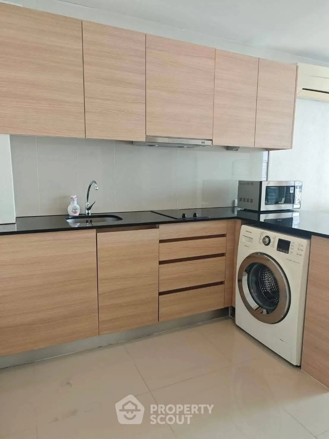 Modern kitchen with wooden cabinets, washing machine, and microwave in sleek apartment.