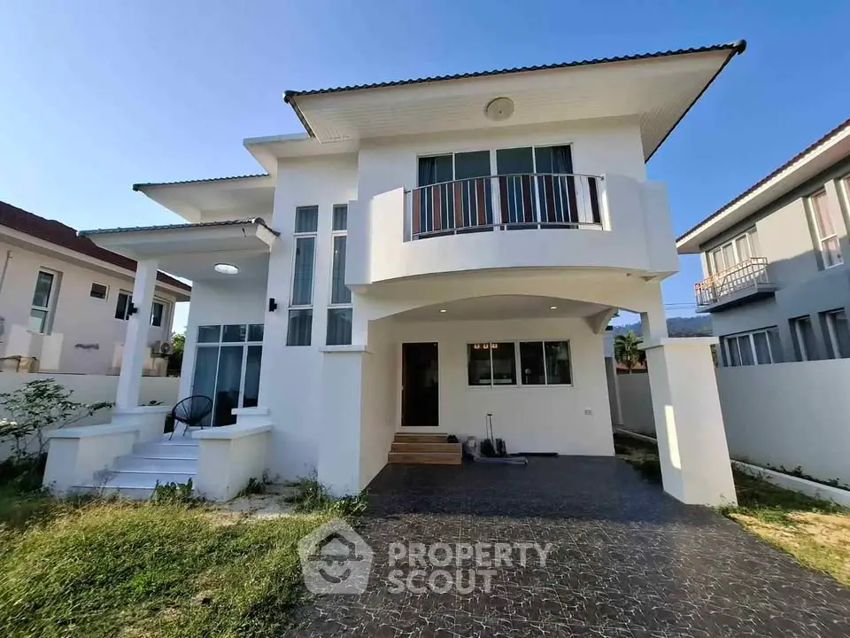 Modern two-story house with balcony and spacious driveway in a serene neighborhood.