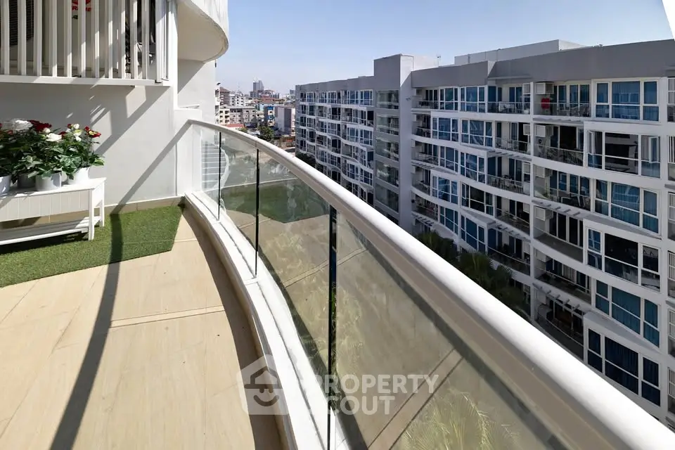 Spacious balcony with glass railing offering stunning city views in modern apartment complex.