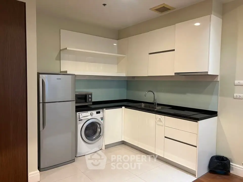 Modern kitchen with sleek cabinets, washing machine, and fridge in a compact layout.