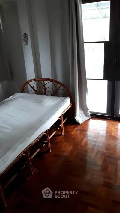 Cozy bedroom with wooden flooring and natural light from large window.