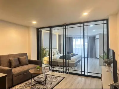 Modern open-layout living room with glass partition to bedroom, featuring stylish decor and natural light.
