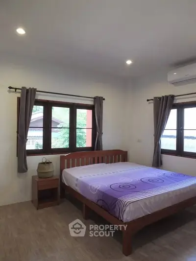 Cozy bedroom with wooden bed frame and large windows offering natural light.