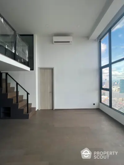 Spacious modern loft with large windows and city view, featuring sleek staircase and minimalist design.