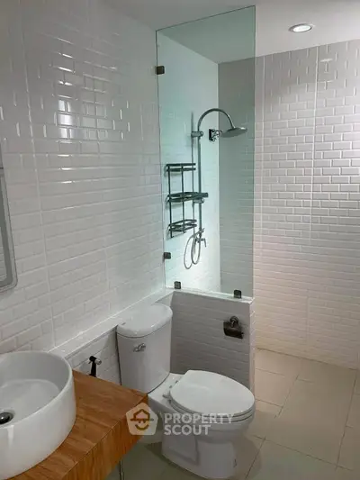 Modern bathroom with glass shower, white tiles, and wooden vanity