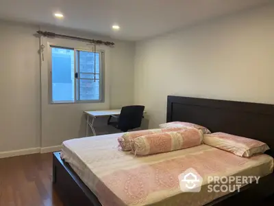 Cozy bedroom with wooden flooring and a study desk by the window in a modern apartment.