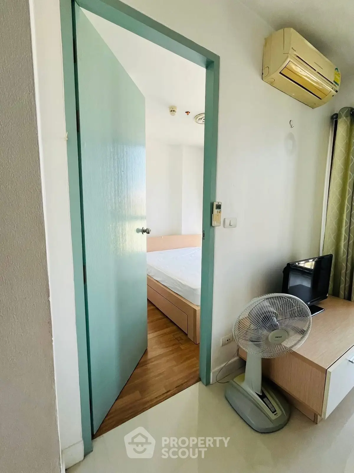 Cozy bedroom with air conditioning and fan, featuring a minimalist design and wooden flooring.