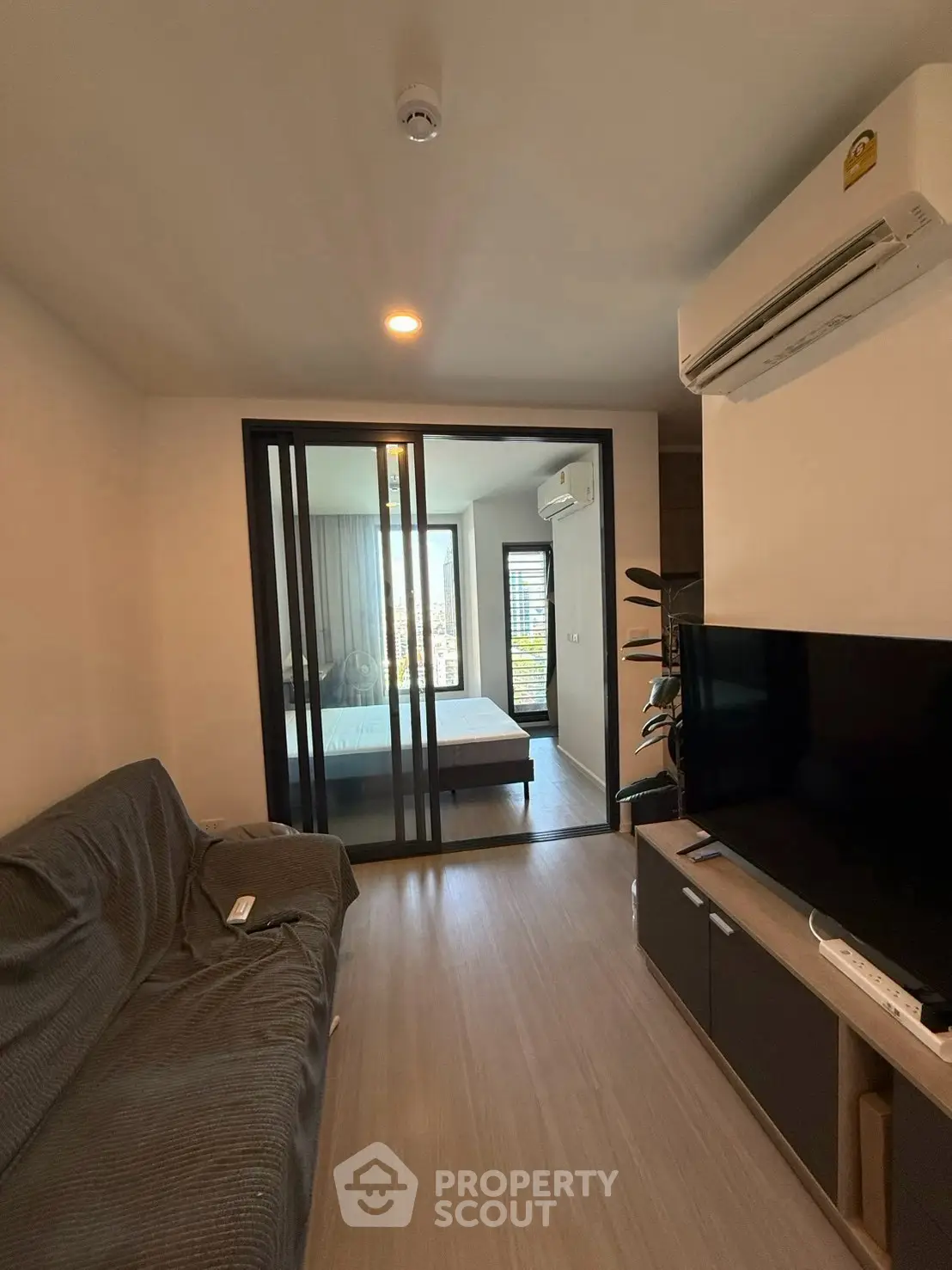 Modern living room with sliding glass doors leading to a cozy bedroom, featuring air conditioning and a sleek TV setup.