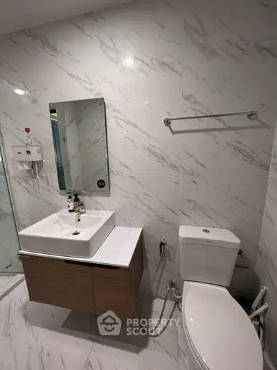 Modern bathroom with sleek fixtures and marble walls, featuring a stylish vanity and toilet.