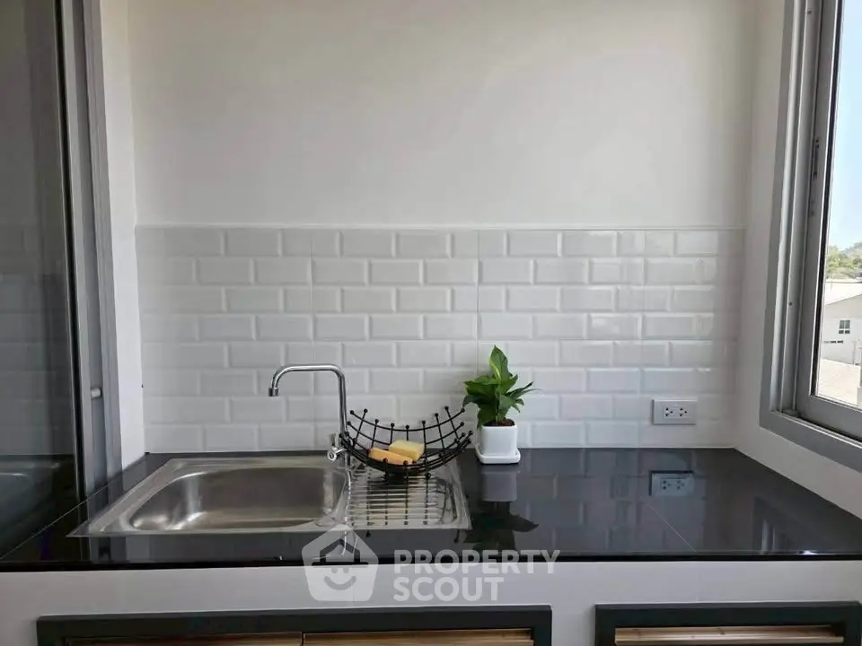 Modern kitchen with sleek black countertop and white subway tile backsplash, featuring a stainless steel sink and large window.