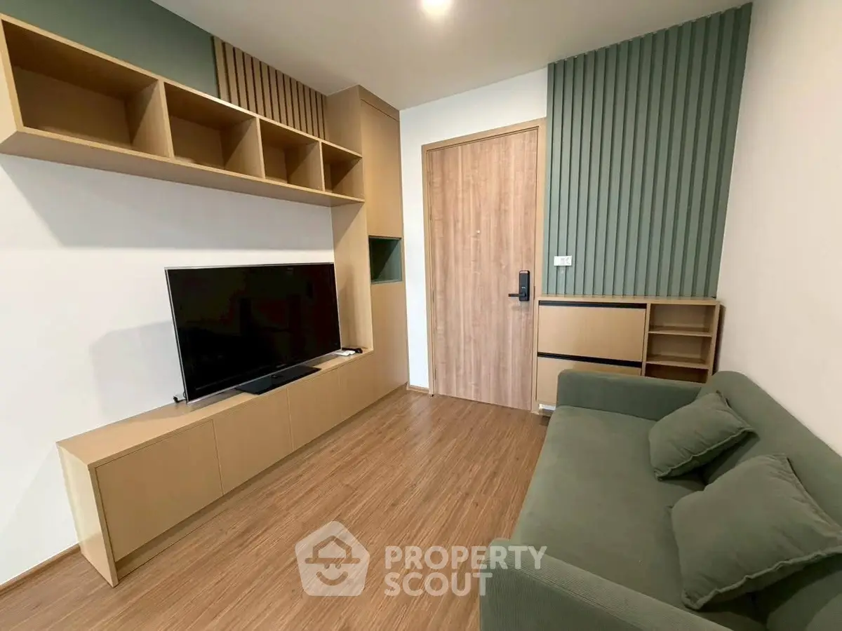 Modern living room with sleek wooden flooring, stylish TV unit, and comfortable green sofa.