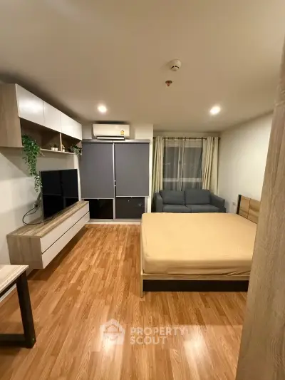 Modern studio apartment with wooden flooring, cozy bed, and stylish entertainment unit.