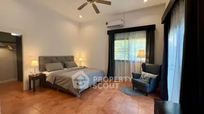 Spacious bedroom with elegant decor and natural light, featuring a cozy armchair and modern ceiling fan.