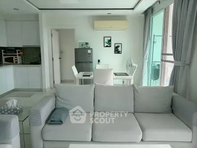 Modern living room with open kitchen, featuring sleek furniture and bright natural lighting.