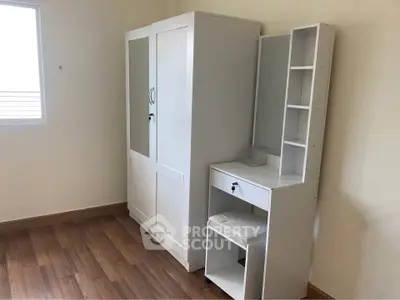 Spacious bedroom with elegant white wardrobe and vanity set on wooden flooring.