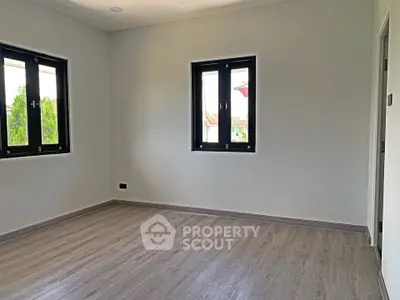 Spacious empty room with large windows and wooden flooring, perfect for customization.