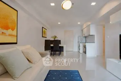Modern living room with sleek kitchen and dining area, featuring elegant decor and bright lighting.
