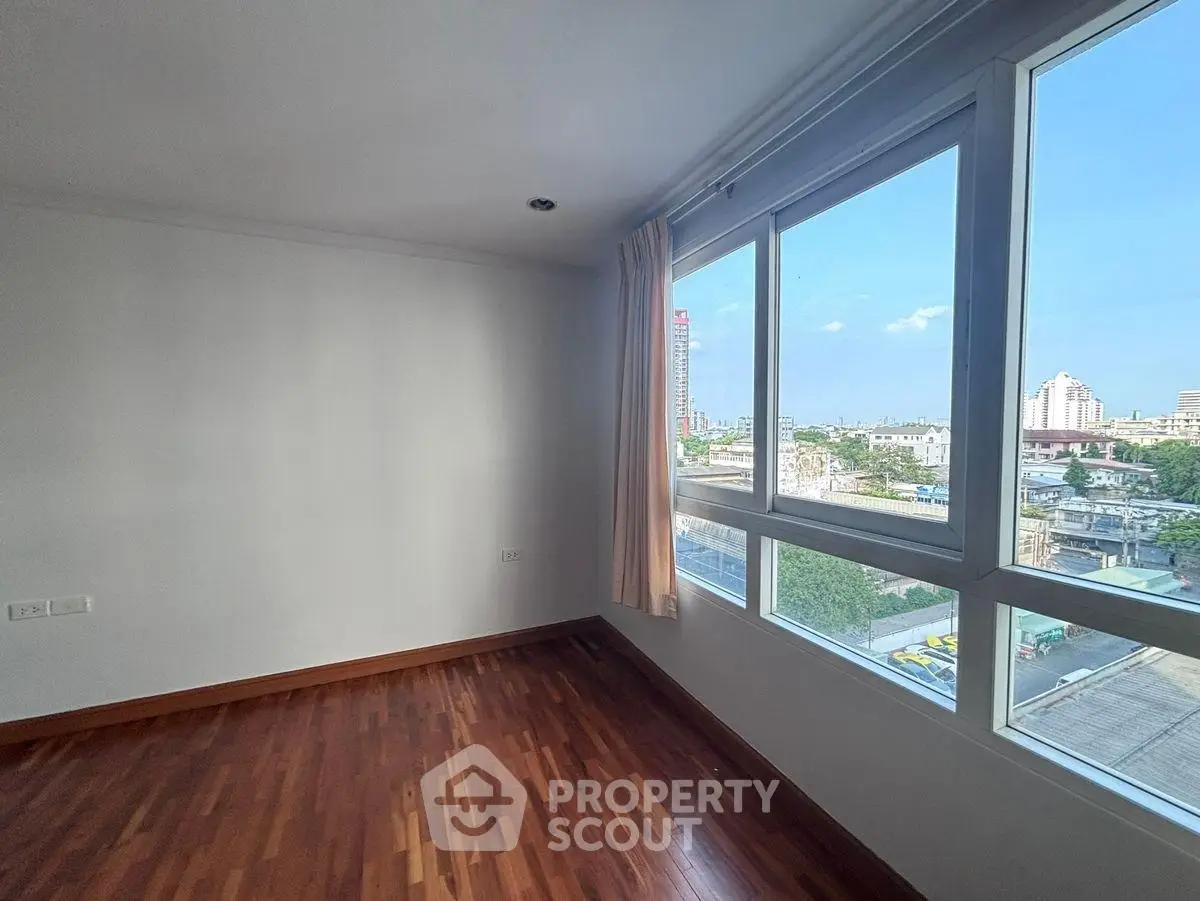 Spacious room with large windows offering a stunning city view and elegant wooden flooring.