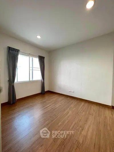 Spacious empty room with wooden flooring and large window, perfect for customization.