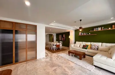Spacious living room with modern decor and open dining area, featuring elegant lighting and stylish furniture.