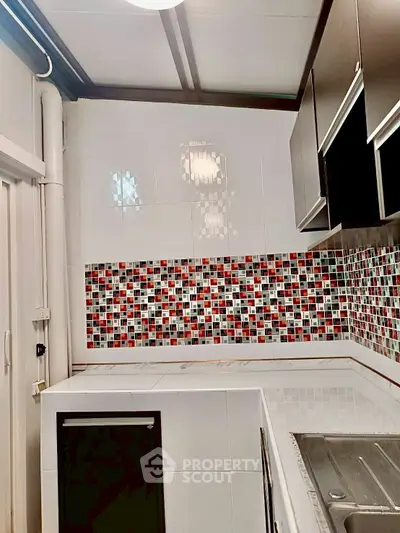Modern kitchen with colorful mosaic backsplash and sleek cabinetry.
